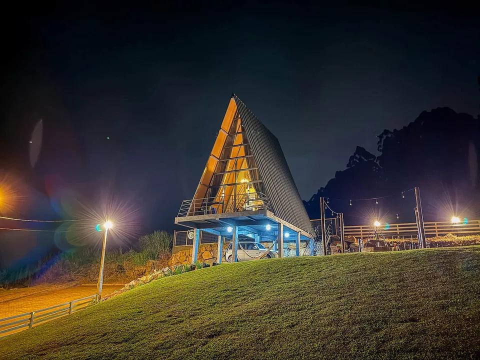 A cabana A-frame iluminada à noite no alto do gramado, com as luzes do caminho acesas