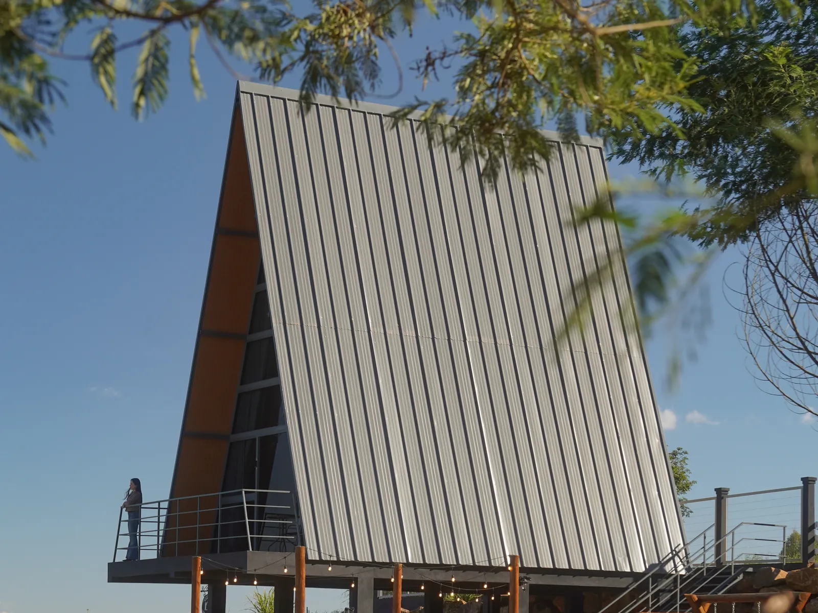Cabana A-frame da Reserva Linha Imperial vista do gramado, com a cerca branca e o firepit sob o deck